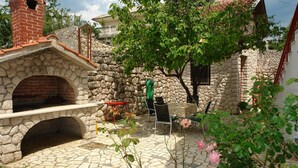 A stone building with a brick chimney, outdoor seating, and a garden with flowering plants. - Apartments Nikolina (Novi Vinodolski)