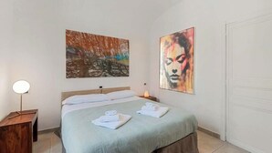A bedroom with a bed, two towels, a bedside lamp, and two paintings on the wall. - Discover your oasis of relaxation in Pitelli, a charming village overlooking the sea! We present you a splendid holiday home ideal for families and groups of up to 4 people.The house consists of two welcoming and tastefully furnished bedrooms, perfect fo (Pitelli)