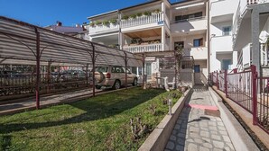 En bostadsbyggnad med flera balkonger, ett takförsett parkeringsområde och en gångstig av sten.
