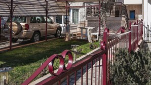 En bostadsbyggnad med en balkong i två våningar, en parkerad SUV och ett rött staket av metall.