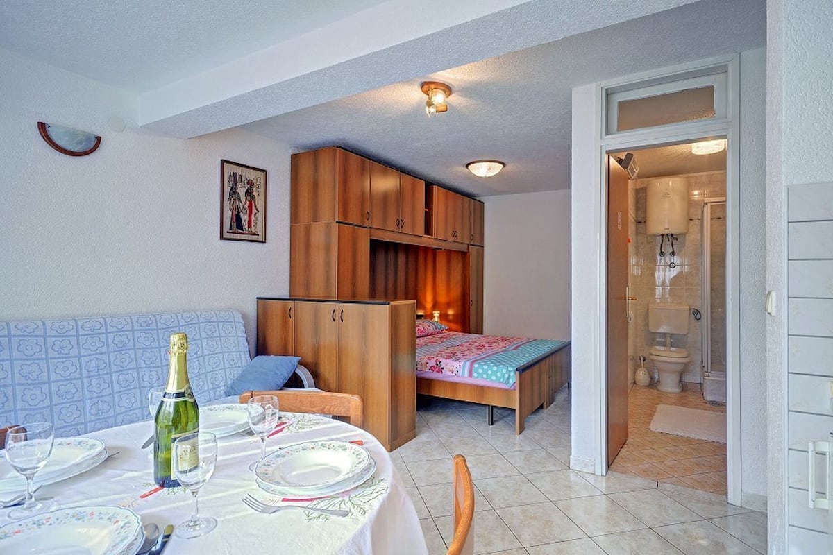 Une chambre à coucher de taille modeste, avec un lit, une armoire en bois et une petite salle de bain visible à travers une porte ouverte.