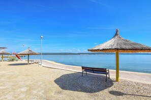 A beach with thatched umbrellas, a bench, and a playground. - House Cvit (Pasman)