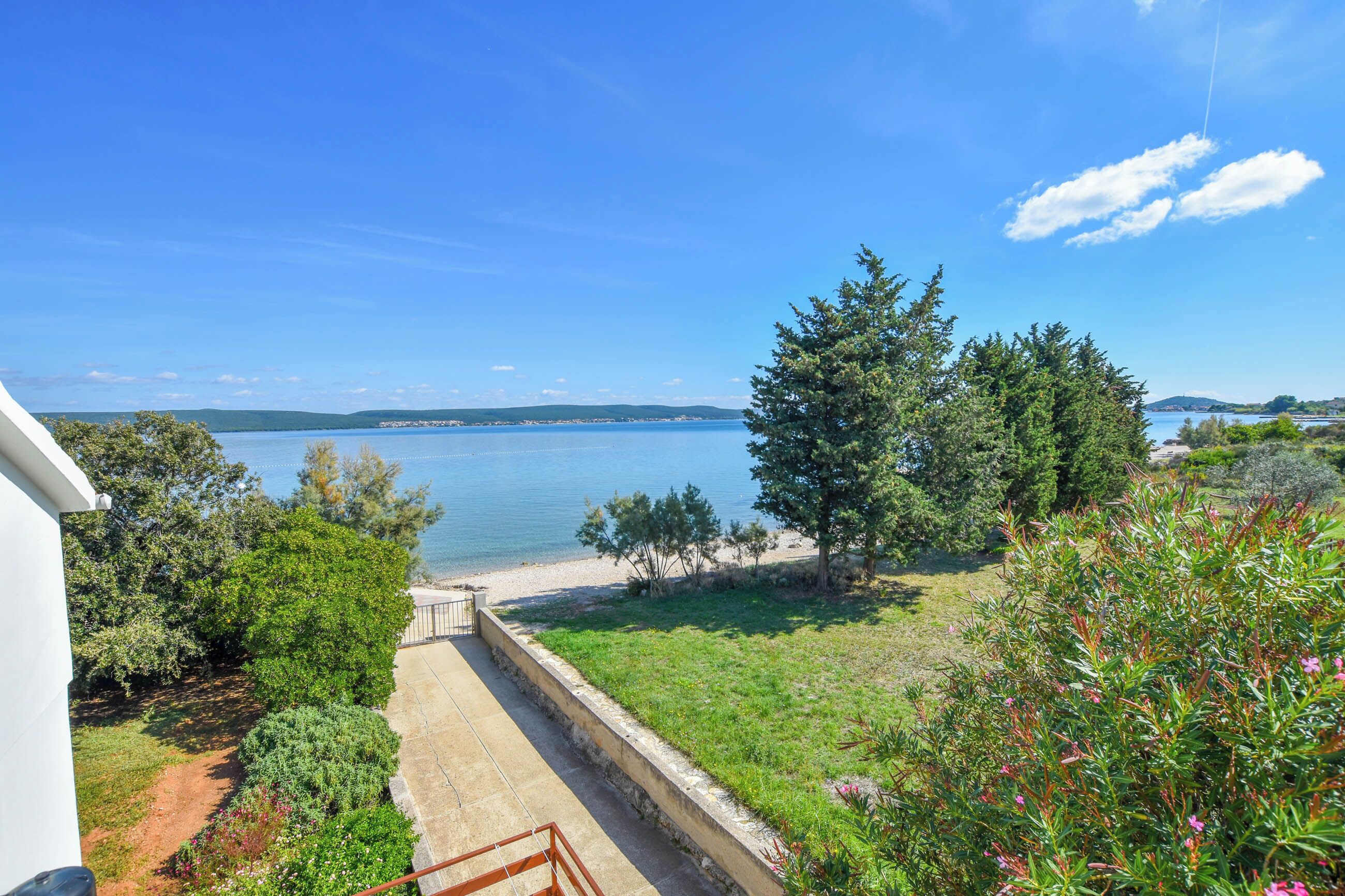 A coastal view with a clear sky, a sandy beach, and a grassy area with trees.