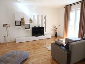 A modern living room with a flat-screen TV on a white console, a grey sofa, and a patterned ottoman. - Apartments Lea-stella (Zadar)