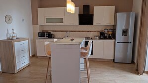 Una cocina moderna con armarios blancos, un refrigerador de acero inoxidable, un microondas y un comedor con mesa de vidrio y dos sillas.