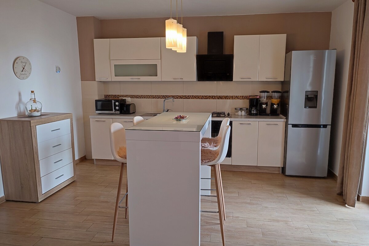 A modern kitchen with white cabinets, a stainless steel refrigerator, a microwave, and a dining area with a glass table and two chairs.
