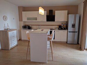 Eine moderne Küche mit weißen Schränken, einem Edelstahlkühlschrank, einer Mikrowelle und einem Essbereich mit einem Glastisch und zwei Stühlen.