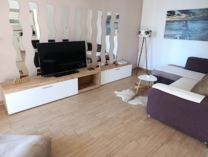 Ein modernes Wohnzimmer mit Flachbildfernseher, einer Holz-Unterhaltungseinrichtung und einem violetten Sofa.