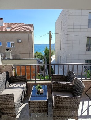 A balcony with wicker furniture and a small table, overlooking a sea view and a street with buildings. - Apartments Lea-stella (Zadar)