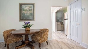 A dining area with a wooden table and two wicker chairs, a framed picture on the wall, and a patterned rug on the floor. - Mariposa Coral Home for 4 (Kerrville)
