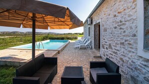 Ein Gebäude aus Stein mit Pool, Sitzgelegenheiten im Freien und Sonnenschirmen.