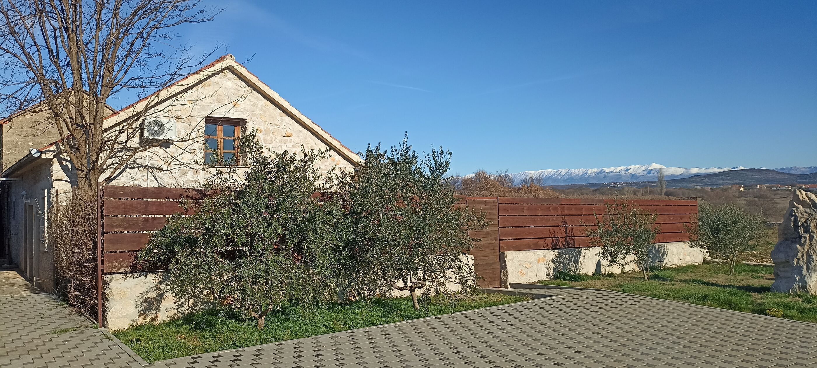 A stone building with a wooden door, a window, and a view of snow-capped mountains.