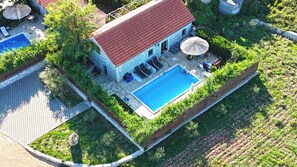 Una vista aerea di una casa con piscina, area relax esterna e giardino.