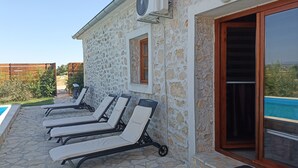 Ein Gebäude aus Stein mit Pool, Liegestühlen im Freien und einem großen Sonnenschirm.