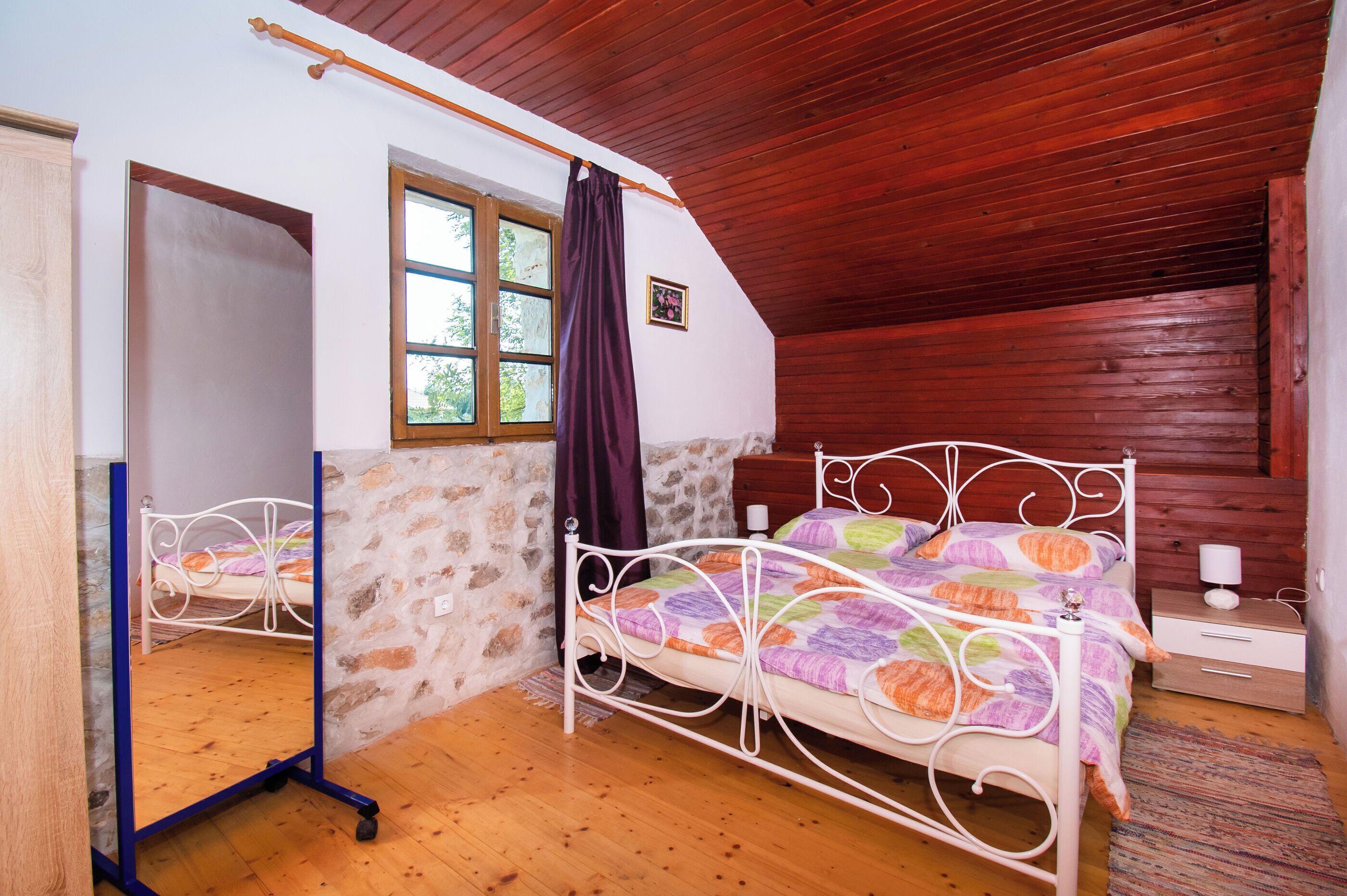 Un dormitorio con cama, techo de madera, pared de piedra y ventana con cortinas.