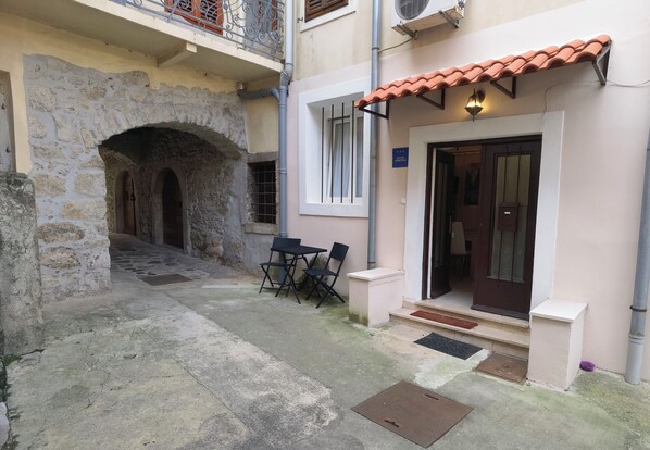 A courtyard with a stone archway, a small table with chairs, and a door with a light fixture. - Apartments Near the sea (Opatija)