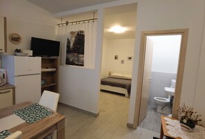 Ett kompakt bostadsutrymme med ett litet kök, en matplats, en säng och ett badrum.