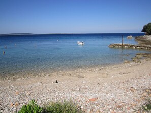 A pebble beach with clear water and a boat anchored in the distance. - Apartment Lumanera Stivan (Cres)