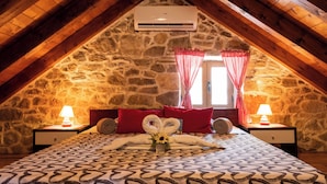 A cozy attic bedroom with a stone wall, a sloped ceiling, and a bed with a patterned bedspread. - House Wood (Orebic)