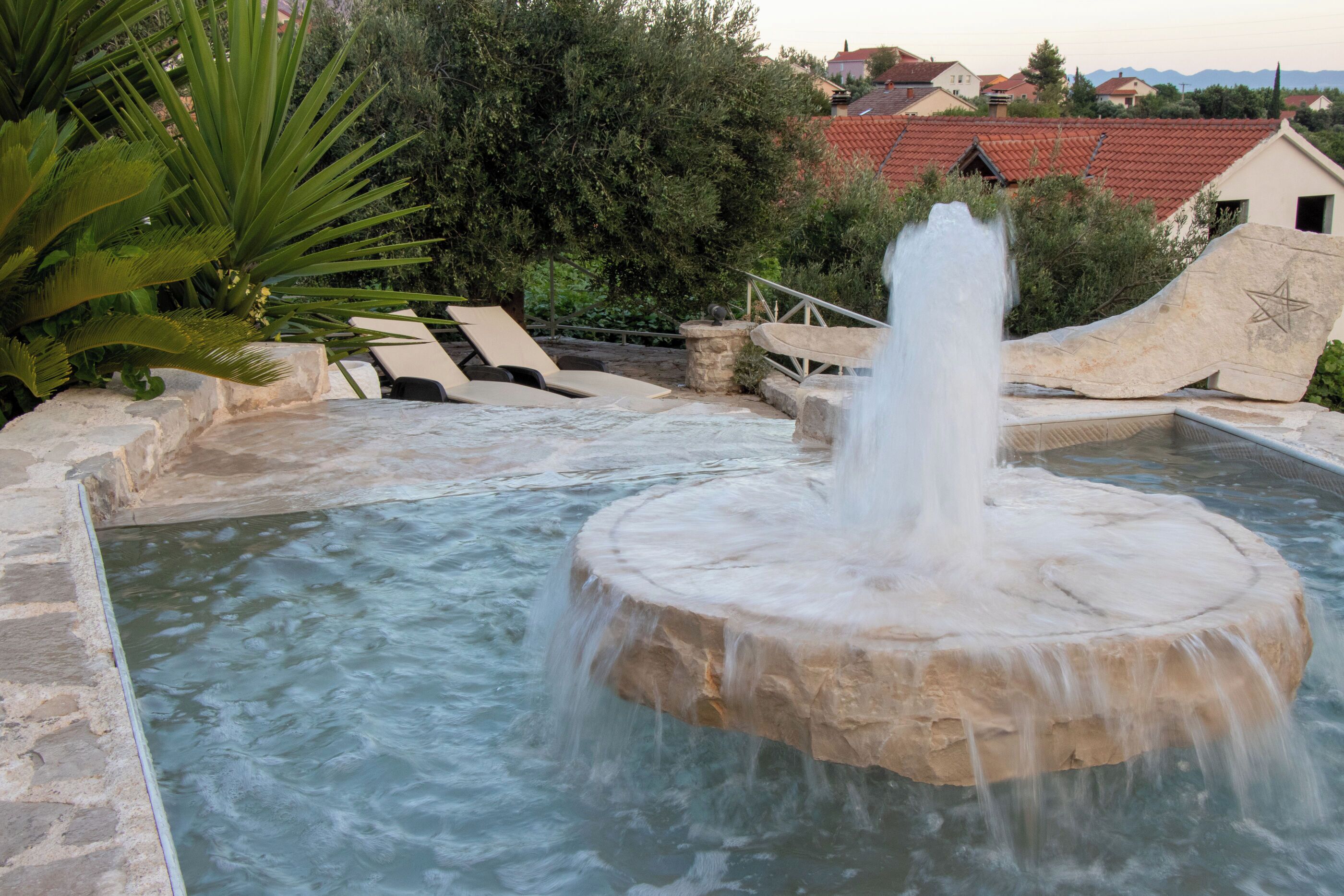 A stone fountain with water spouting from its center, surrounded by a pool and stone steps leading down to the water.