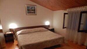 Ett sovrum med en säng, två sängbord, ett litet bord, ett träpanelat tak, en inramad tavla på väggen och ett fönster med gardiner.