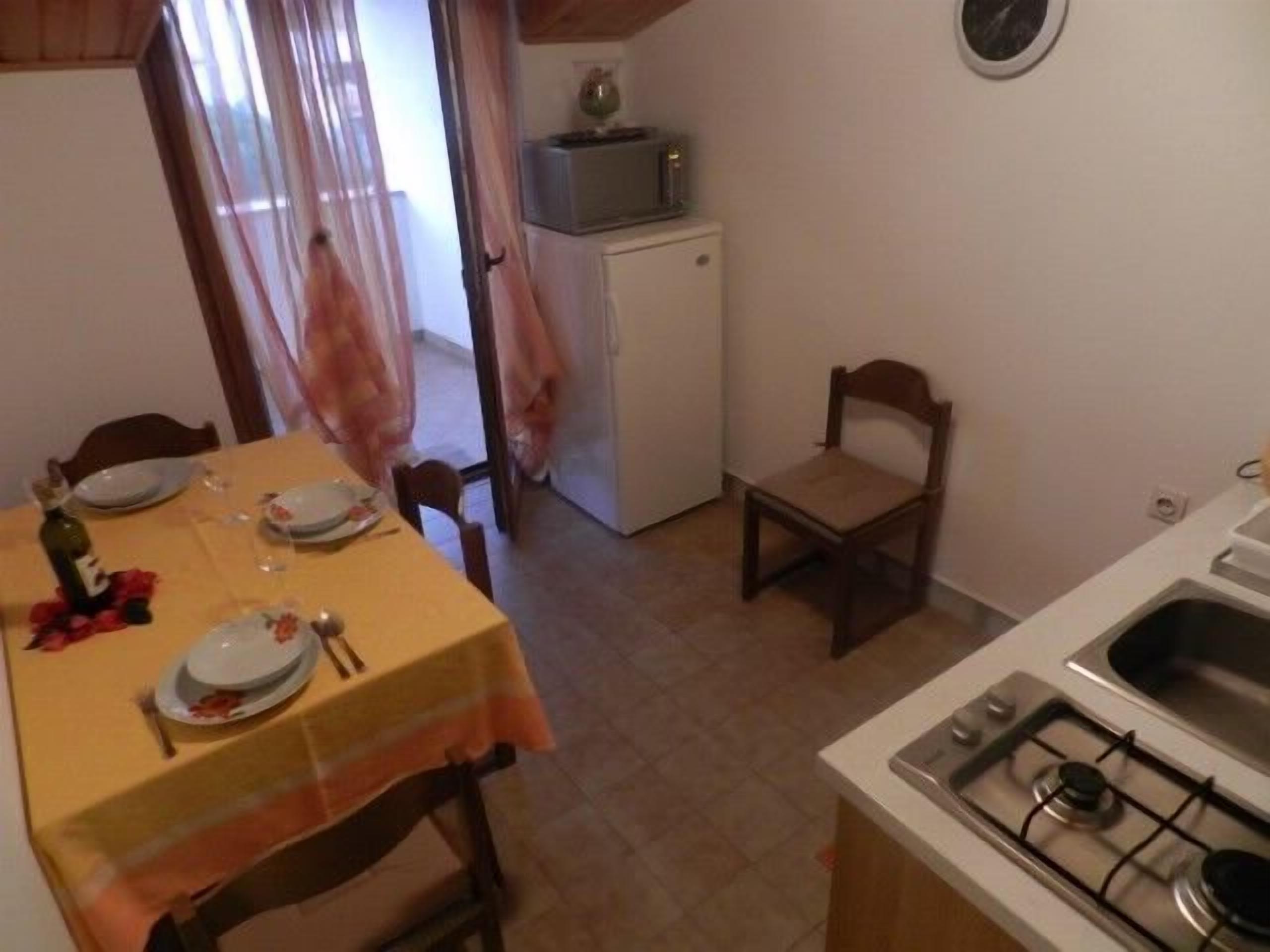 A compact kitchen with a dining table set for two, a refrigerator, a microwave, and a gas stove.