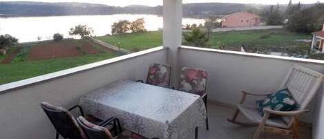 Un balcon avec une table et des chaises, donnant sur un lac et une végétation luxuriante.