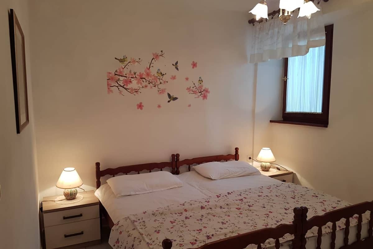 Une chambre à coucher avec un lit en bois, deux tables de chevet avec des lampes, une couvre-lit à motifs floraux et une décoration murale représentant des oiseaux et des fleurs.