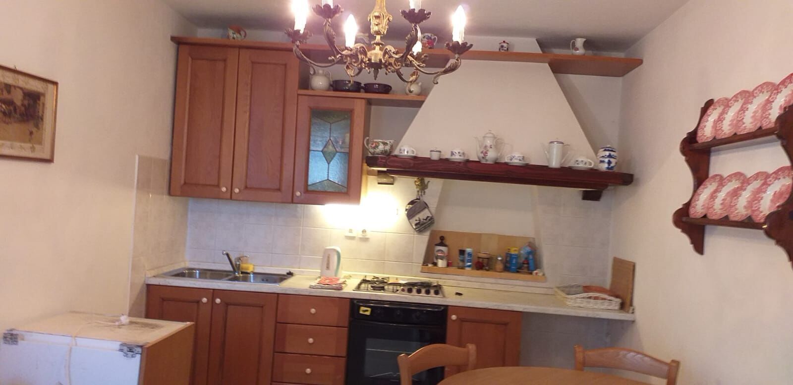 A compact kitchen with wooden cabinets, a gas stove, a sink, and a chandelier.