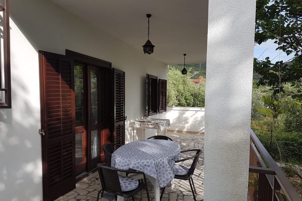Un balcon avec une table et des chaises, une lanterne suspendue et une vue sur la verdure.