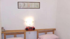 Ein kleines, schlichtes Zimmer mit zwei Einzelbetten, einer Wandleuchte und einem gerahmten Bild über den Betten.