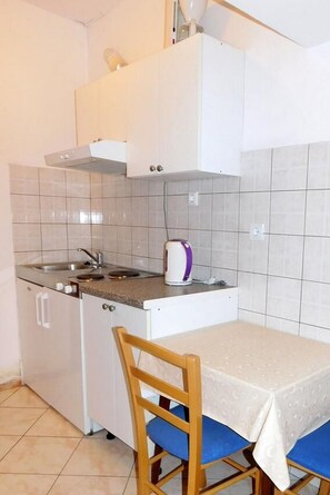 A compact kitchen with white cabinets, a gas stove, a sink, and a table with blue chairs. - Apartments Ljiljana (Smokvica)