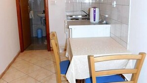 Ένας μικρός και λειτουργικός χώρος κουζίνας με τραπέζι και καρέκλες για φαγητό, ένα λευκό ντουλάπι πάνω από τον νεροχύτη και μια επιφάνεια τοίχου επενδυμένη με πλακάκια.