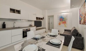 Una cocina moderna con armarios blancos, horno empotrado y comedor con una mesa de mármol dispuesta para cuatro.