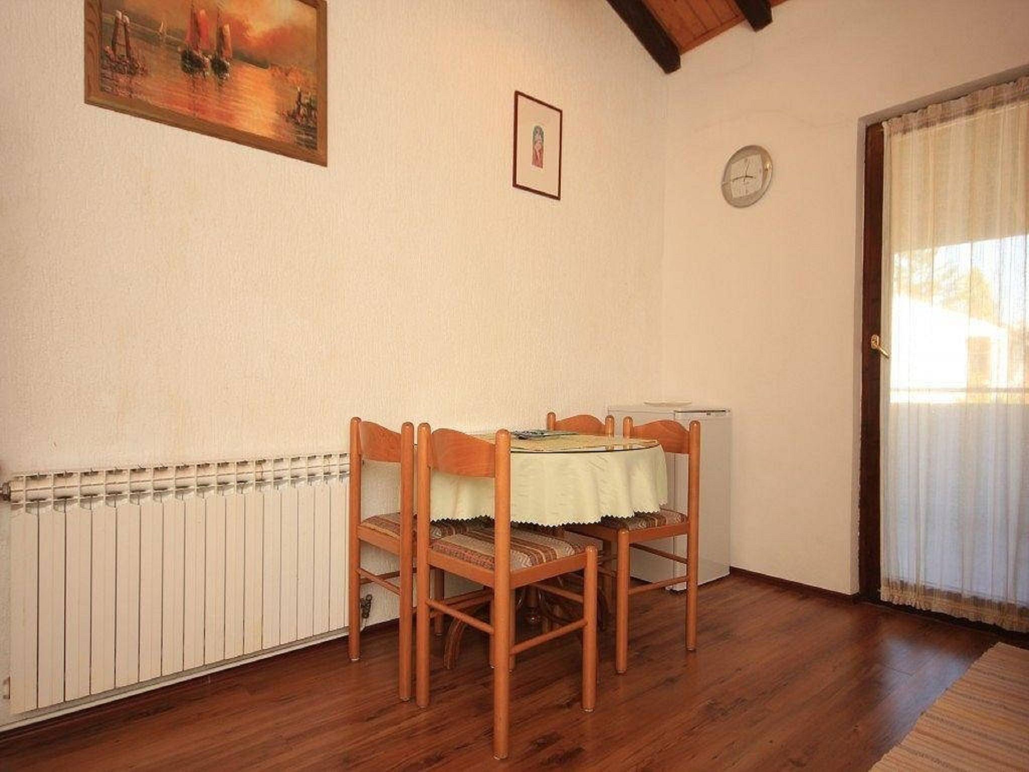 A dining area with a table and chairs, a radiator, a clock, and a painting on the wall.