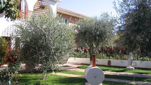 A courtyard with olive trees, a stone sculpture, and a building with a tiled roof. - Apartments Matohanac (Fazana)