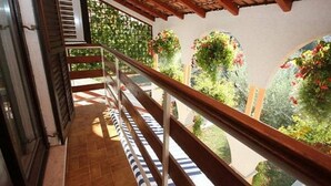 A balcony with a wooden railing, a tiled floor, and a view of a garden with plants and flowers. - Apartments Matohanac (Fazana)