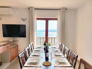 Un espace repas avec vue sur la mer, une télévision et un comptoir en bois.