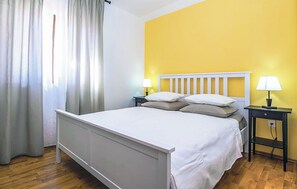 A bedroom with a white bed, two bedside tables with lamps, a window with white curtains, and a yellow wall. - House Majda (Nerezise)