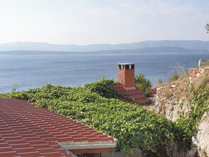 A coastal building with a red-tiled roof, a brick chimney, and lush greenery. - House Majda (Nerezise)