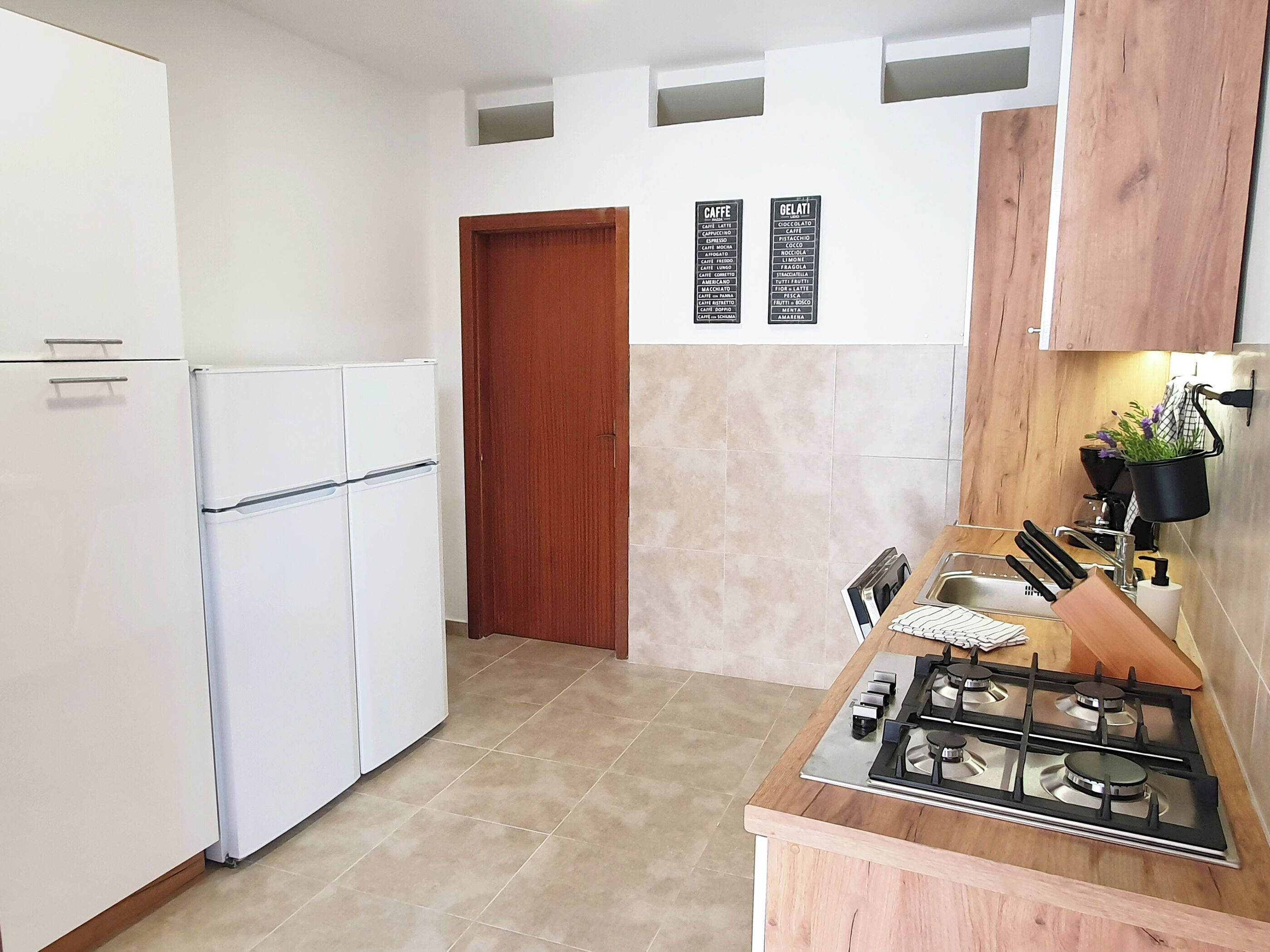A kitchen with a white refrigerator, a wooden door, a gas stove, and a wall-mounted menu board.