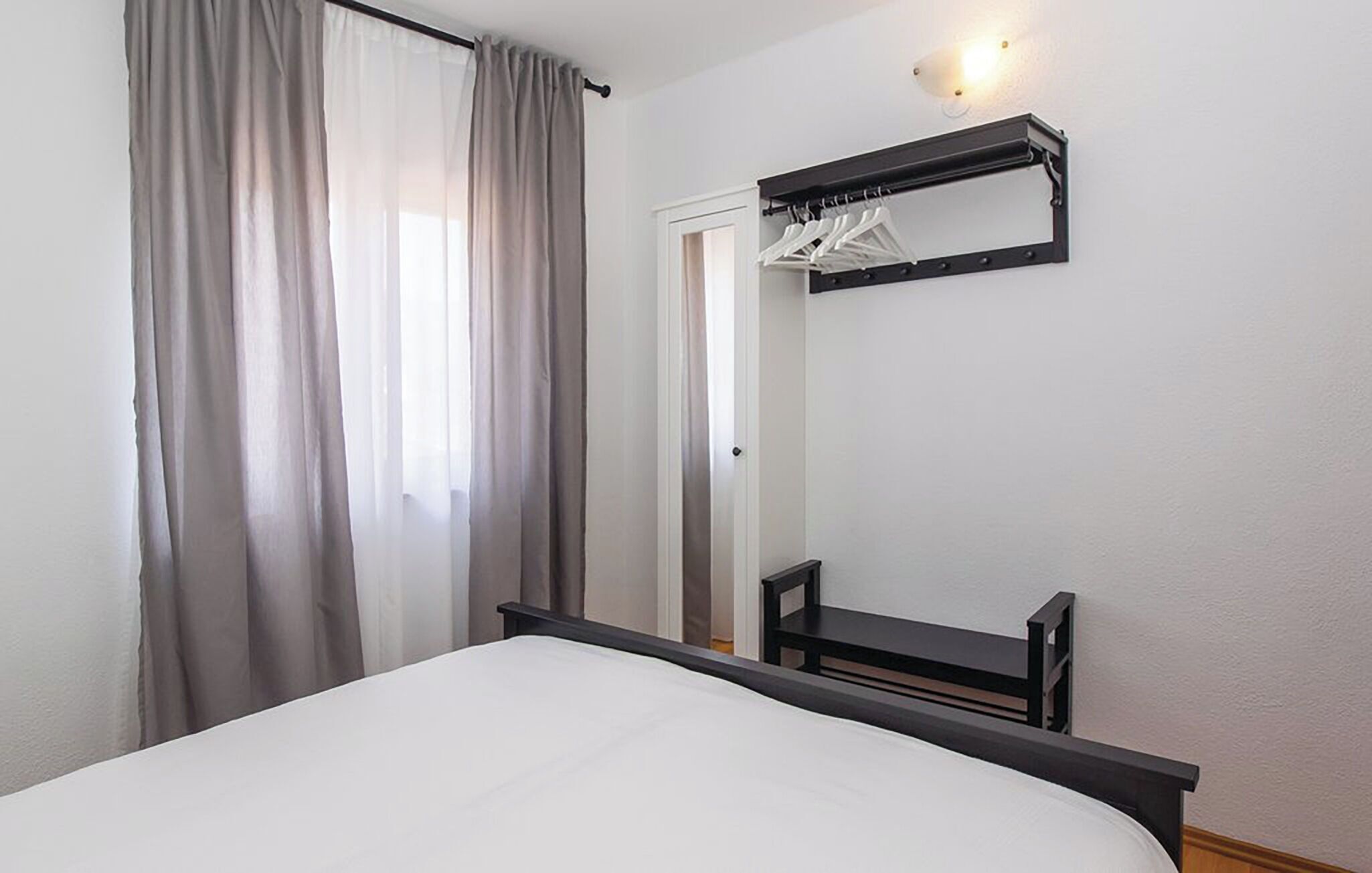 A bedroom with a bed, a mirror, a coat rack, and a door.
