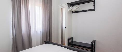 A bedroom with a bed, a mirror, a coat rack, and a door.