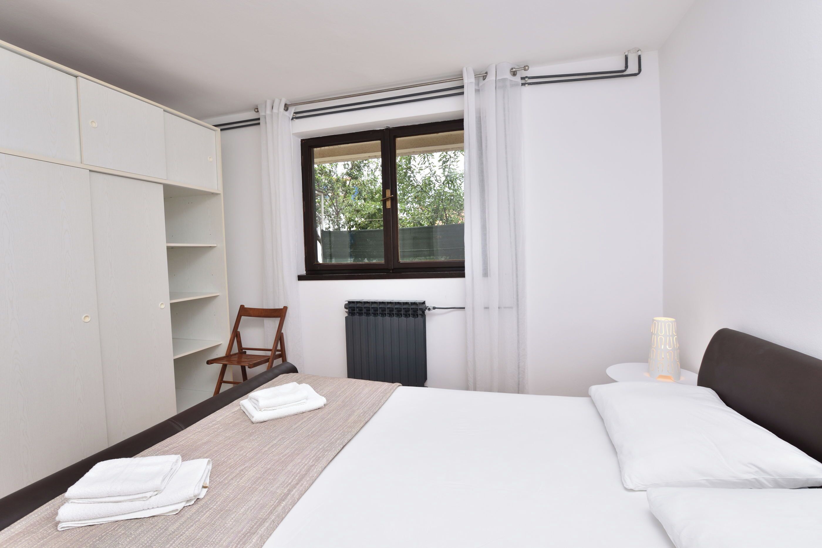 A bedroom with a bed, a chair, a wardrobe, and a window with curtains.