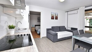 Eine moderne Küche mit einem schwarzen Herd, einer Spüle und einem weißen Schrank. Im Wohnbereich befindet sich ein graues Sofa und ein Esstisch mit Stühlen.