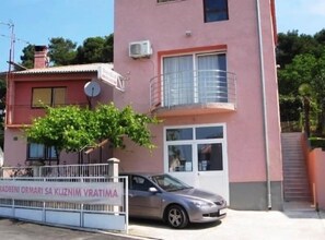 Un edificio rosa con un coche estacionado frente a él, un cartel que dice "RADBENI ORMARI SA KUZNIM VRATIMA" y una escalera que lleva a la entrada.