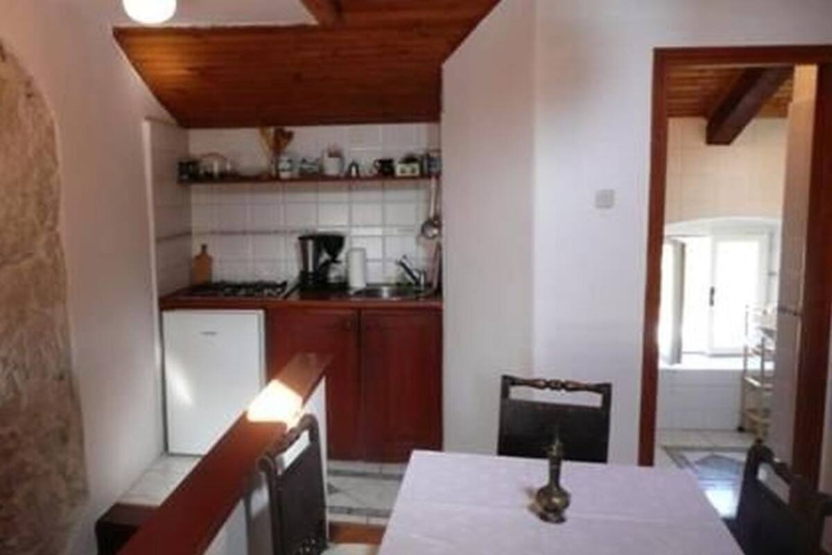 A compact kitchen with a refrigerator, stove, and wooden cabinets. A dining table with chairs is positioned in front of the kitchen.