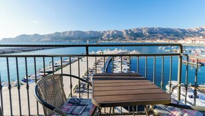 A balcony with a table and chairs overlooking a marina with boats and a mountainous backdrop. - Apartment Jasna By the sea (Baska)