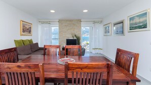 A dining area with a wooden table and chairs, a sofa, and a television. - Apartment Jasna By the sea (Baska)