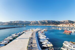 A marina with boats docked along a curved pier, a clear sky, and a mountainous backdrop. - Apartment Jasna By the sea (Baska)
